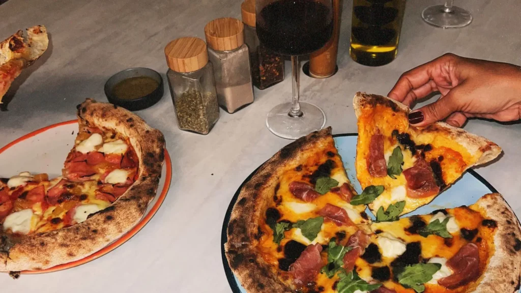 Table with gourmet pizzas and a glass of wine at OSH Hotel Getsemaní restaurant