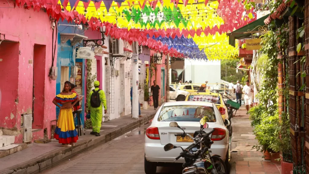 Calle colorida en Getsemaní Cartagena con banderines festivos, casas coloniales, locales y turistas caminando por el barrio histórico.